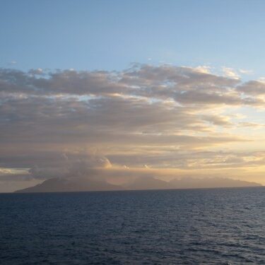 Distant island under cloudy sunset sky.