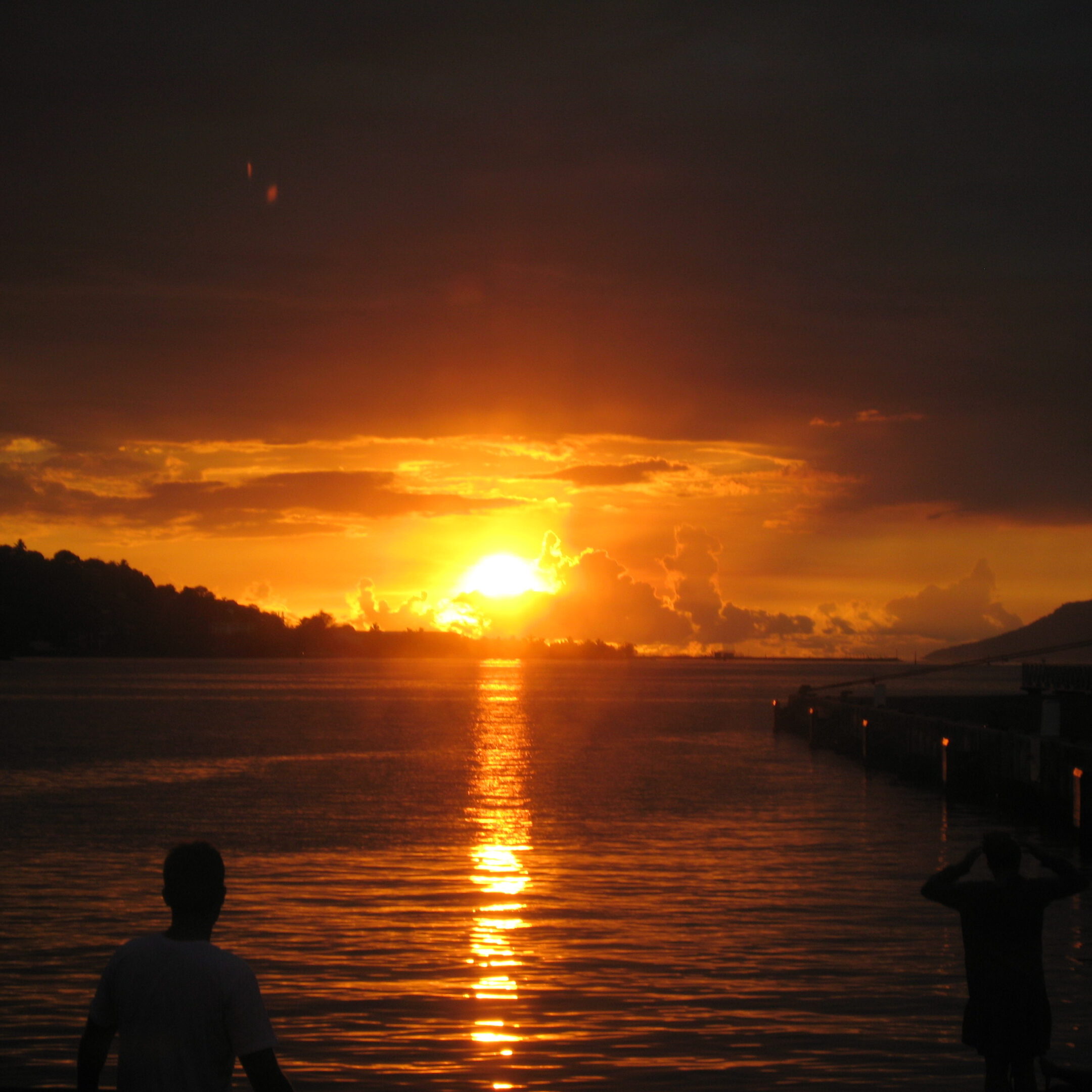Sunset over calm water with silhouettes.