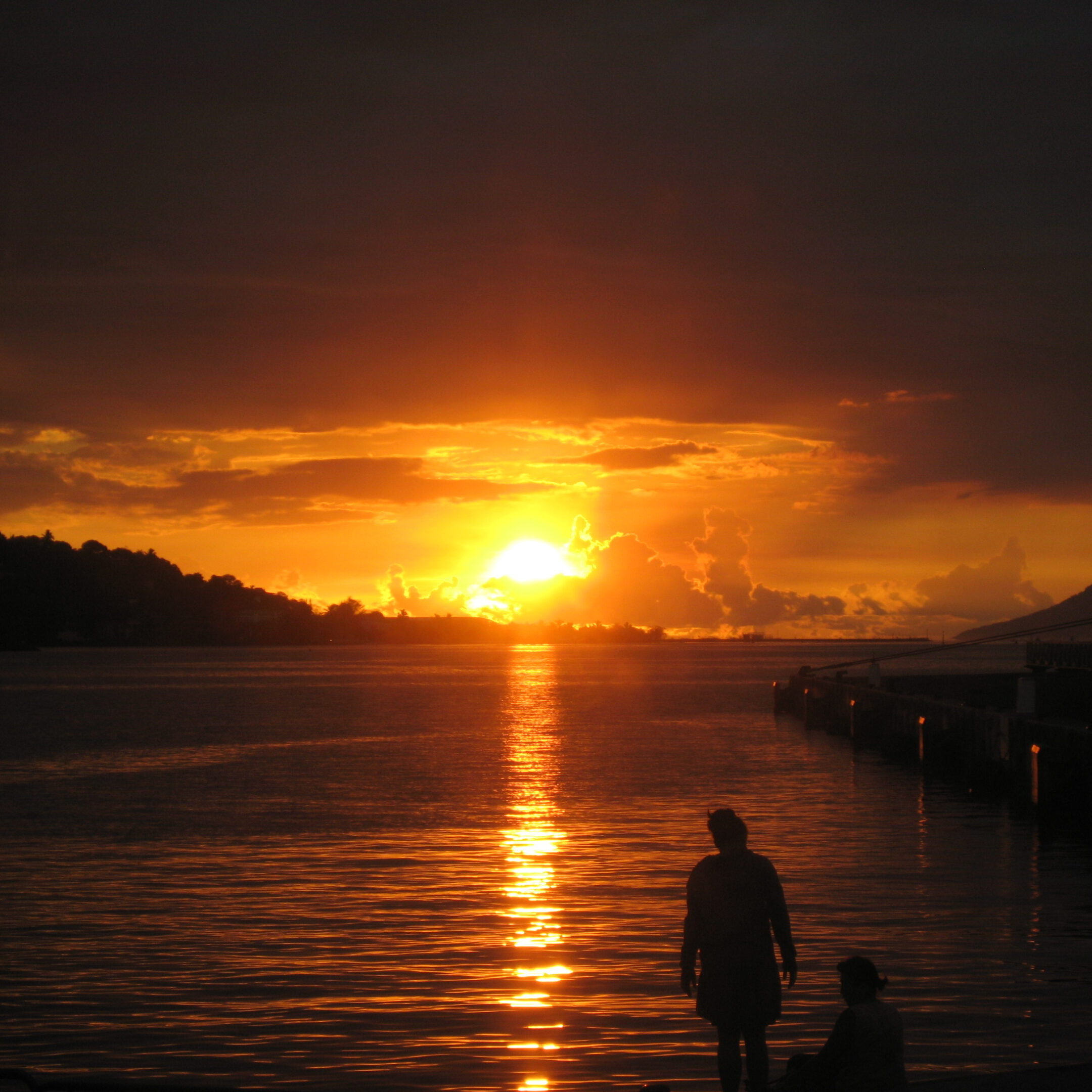 Sunset over water with silhouetted figures.