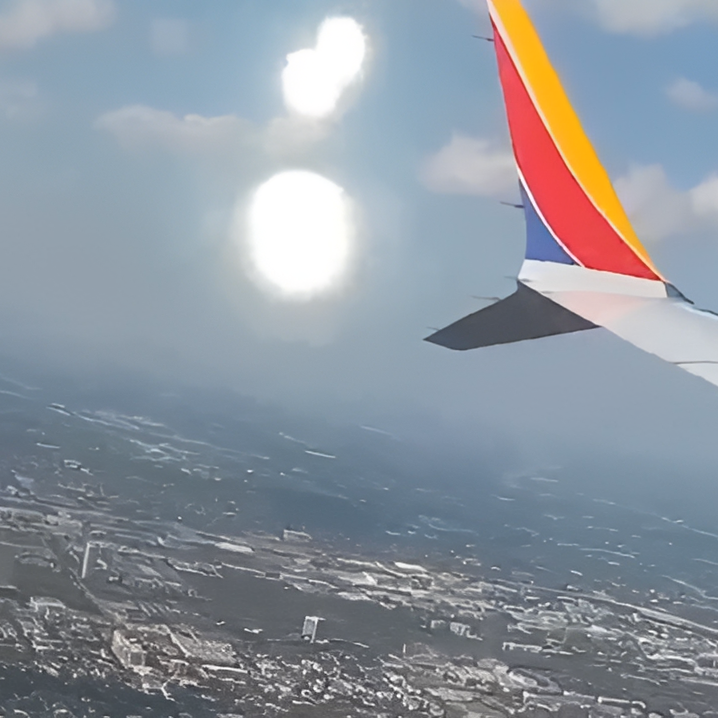 Airplane wing over cityscape with bright reflections.