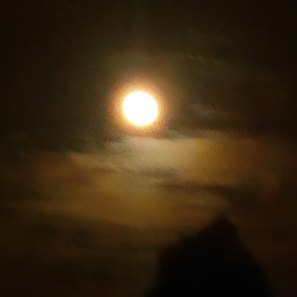 Full moon glowing through cloudy night sky